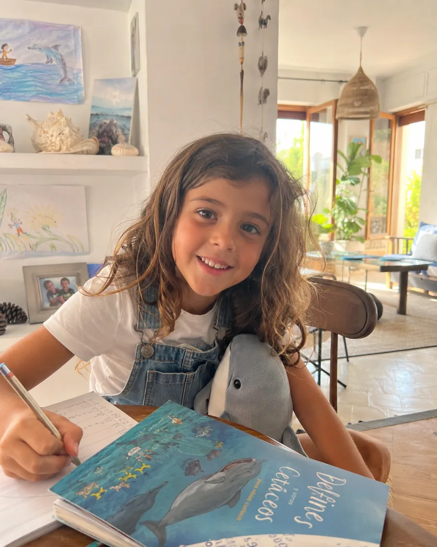 Foto de referencia de Olivia con pelo castaño ondulado, peto vaquero y un libro sobre el mar
